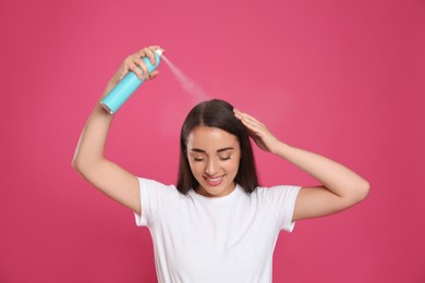 Young woman applying dry shampoo against pink background