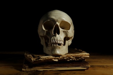 Photo of Human skull and old book on wooden table against black background