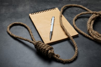 Photo of Rope noose and blank notebook with pen on grey table