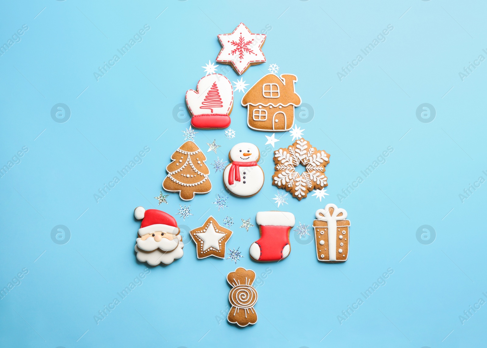 Photo of Delicious gingerbread cookies arranged in shape of Christmas tree on light blue background, flat lay