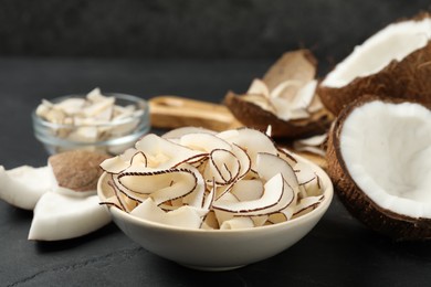 Photo of Tasty coconut chips in bowl on black table