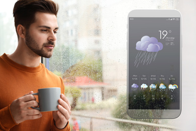 Image of Thoughtful handsome man near window indoors and smartphone with open weather forecast app 