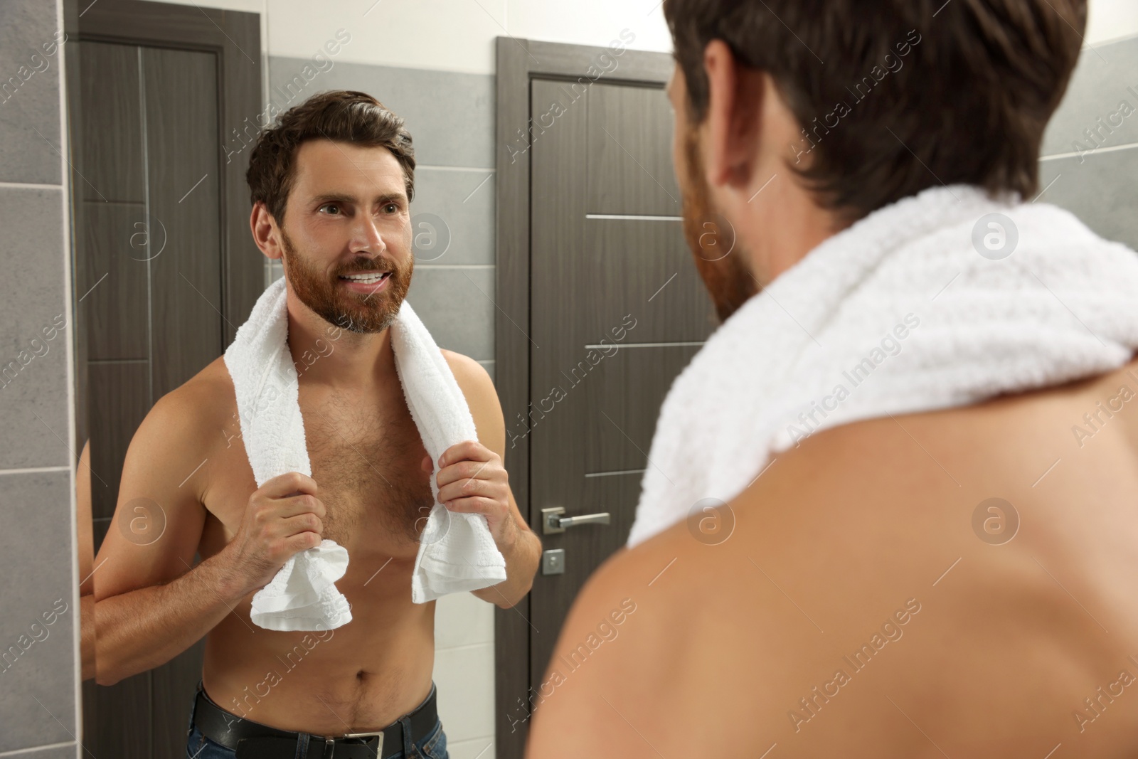 Photo of Handsome bearded man looking at mirror in bathroom near wooden doors