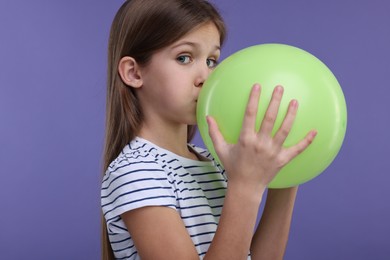 Photo of Girl inflating light green balloon on violet background