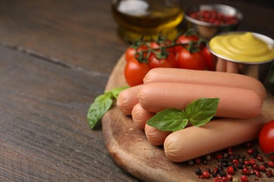 Photo of Delicious boiled sausages, basil and peppercorns on wooden table, closeup. Space for text