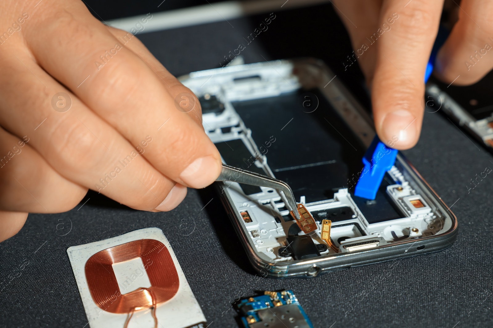 Photo of Technician repairing broken smartphone at table, closeup