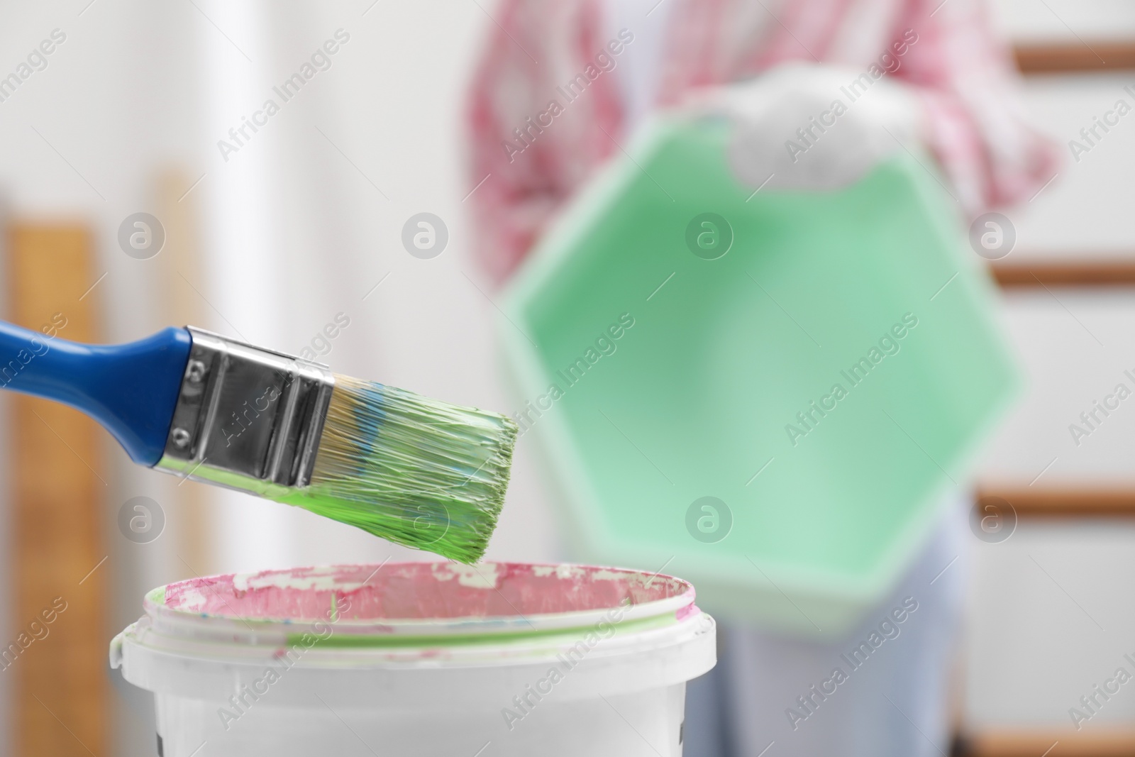 Photo of Brush with green paint above bucket indoors, closeup. Space for text
