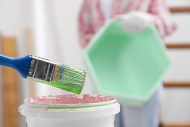 Photo of Brush with green paint above bucket indoors, closeup. Space for text