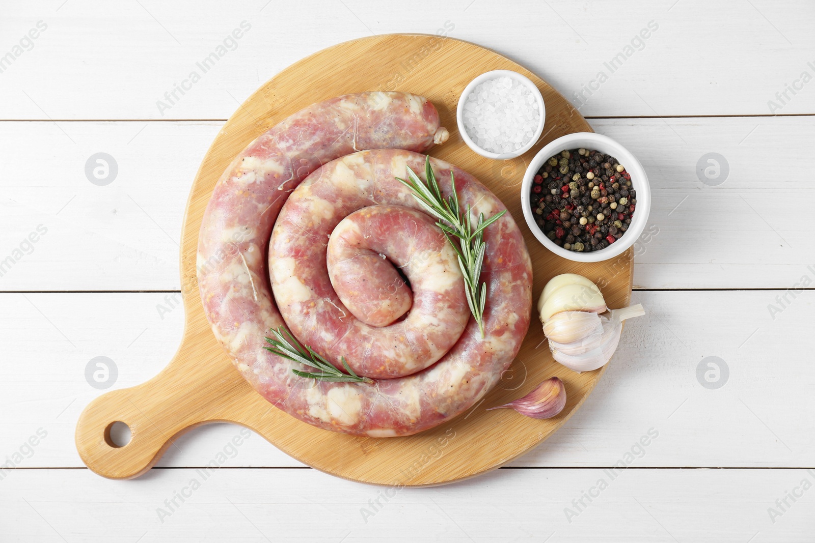 Photo of Raw homemade sausage, garlic and spices on white wooden table, top view