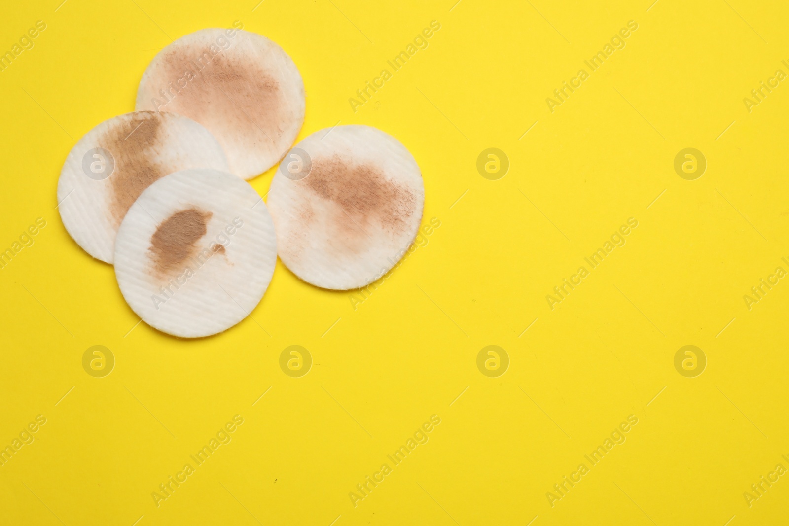 Photo of Dirty cotton pads after removing makeup on yellow background, flat lay. Space for text