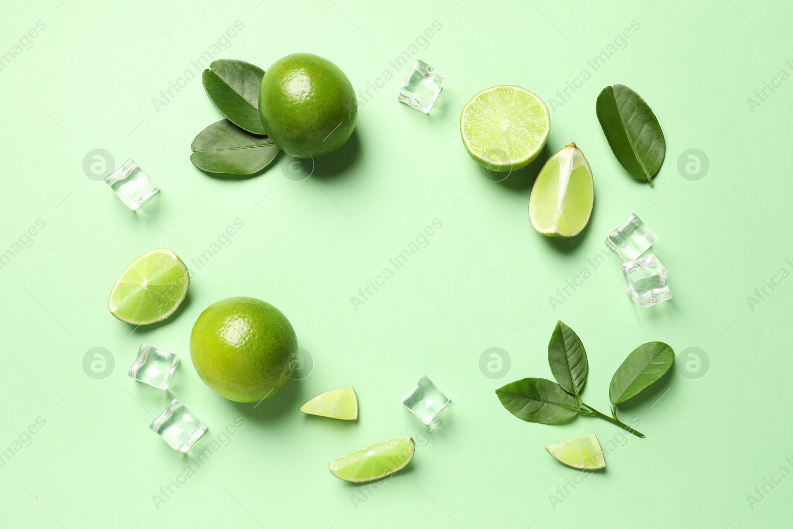 Photo of Frame made of ripe limes with leaves and ice cubes on light green background, flat lay