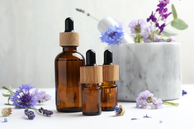 Aromatherapy. Essential oils, flowers, mortar and pestle on white table