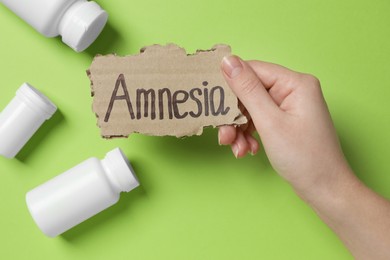 Photo of Woman holding piece of cardboard with word Amnesia on light green background, top view