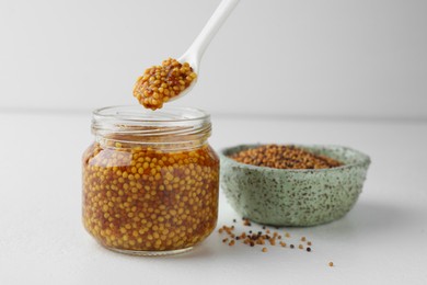 Photo of Taking whole grain mustard with spoon from jar on white table