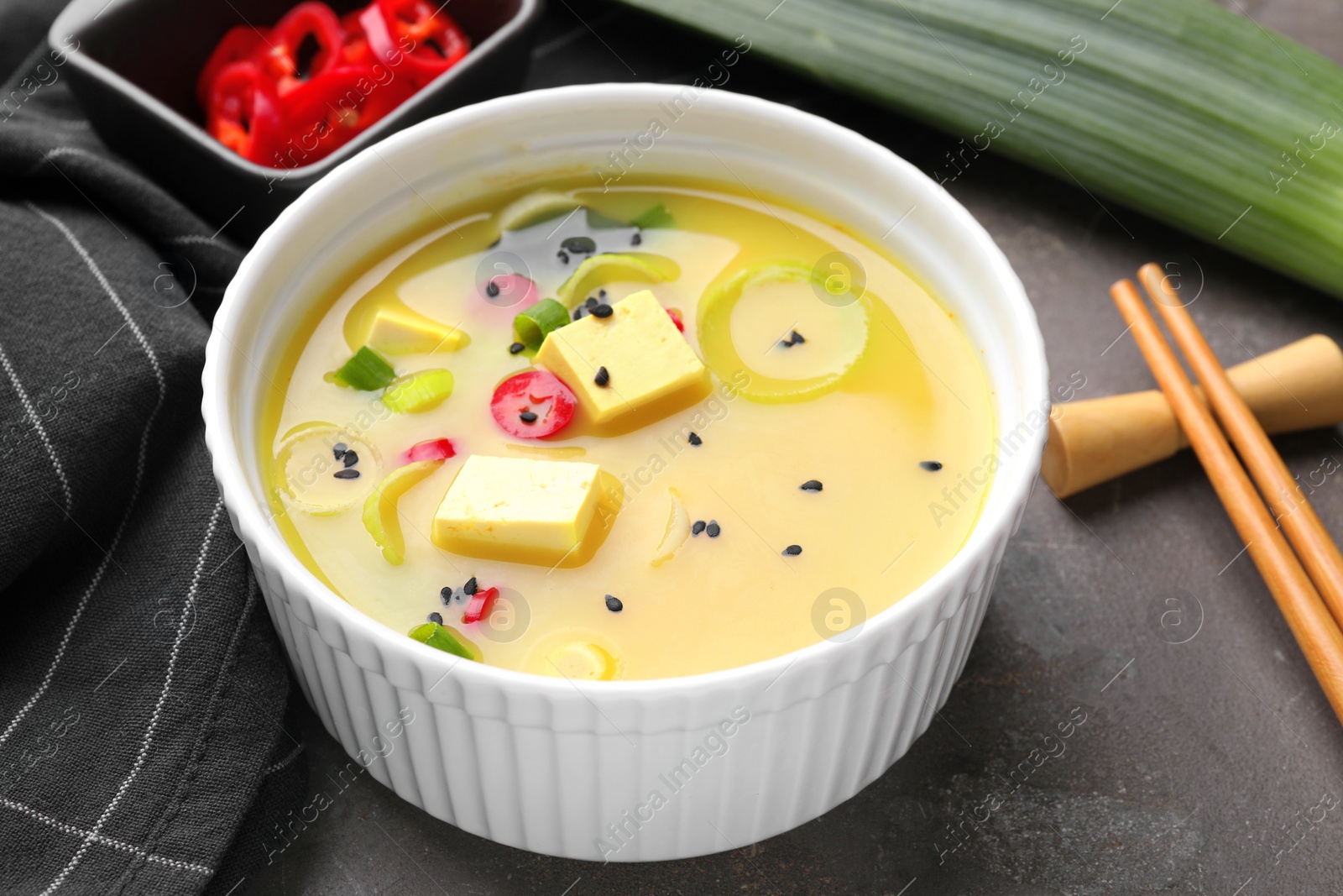 Photo of Bowl of delicious miso soup with tofu served on grey table, closeup