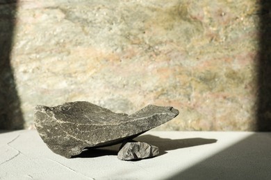 Photo of Presentation of product. Podium made of stones on light textured table. Space for text