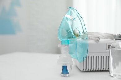 Photo of Modern nebulizer with face mask and medicine on white table indoors, space for text. Inhalation equipment