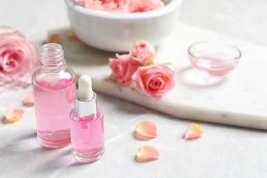 Photo of Bottles of rose essential oil and fresh flowers on table, space for text