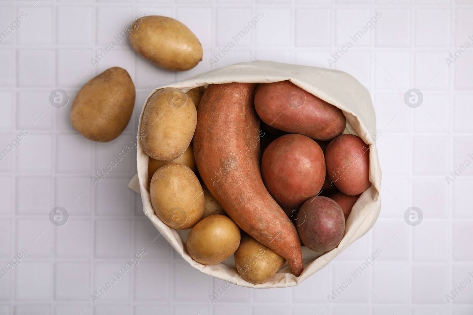 Photo of Different types of fresh potatoes in bag on white table, top view