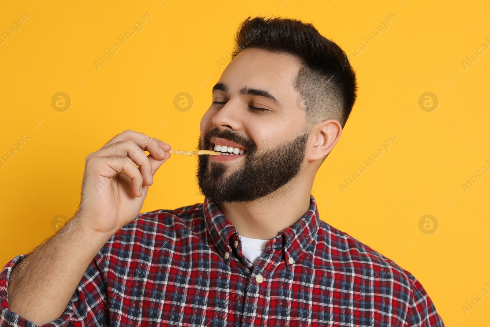 Photo of Young man eating French fries on orange background