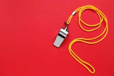 Photo of One metal whistle with cord on red background, top view. Space for text