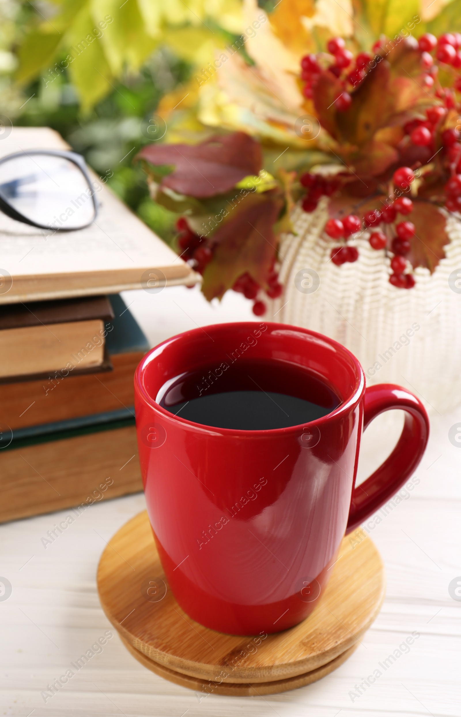 Photo of Cup with hot drink, stack of books and viburnum on white wooden windowsill indoors. Autumn atmosphere