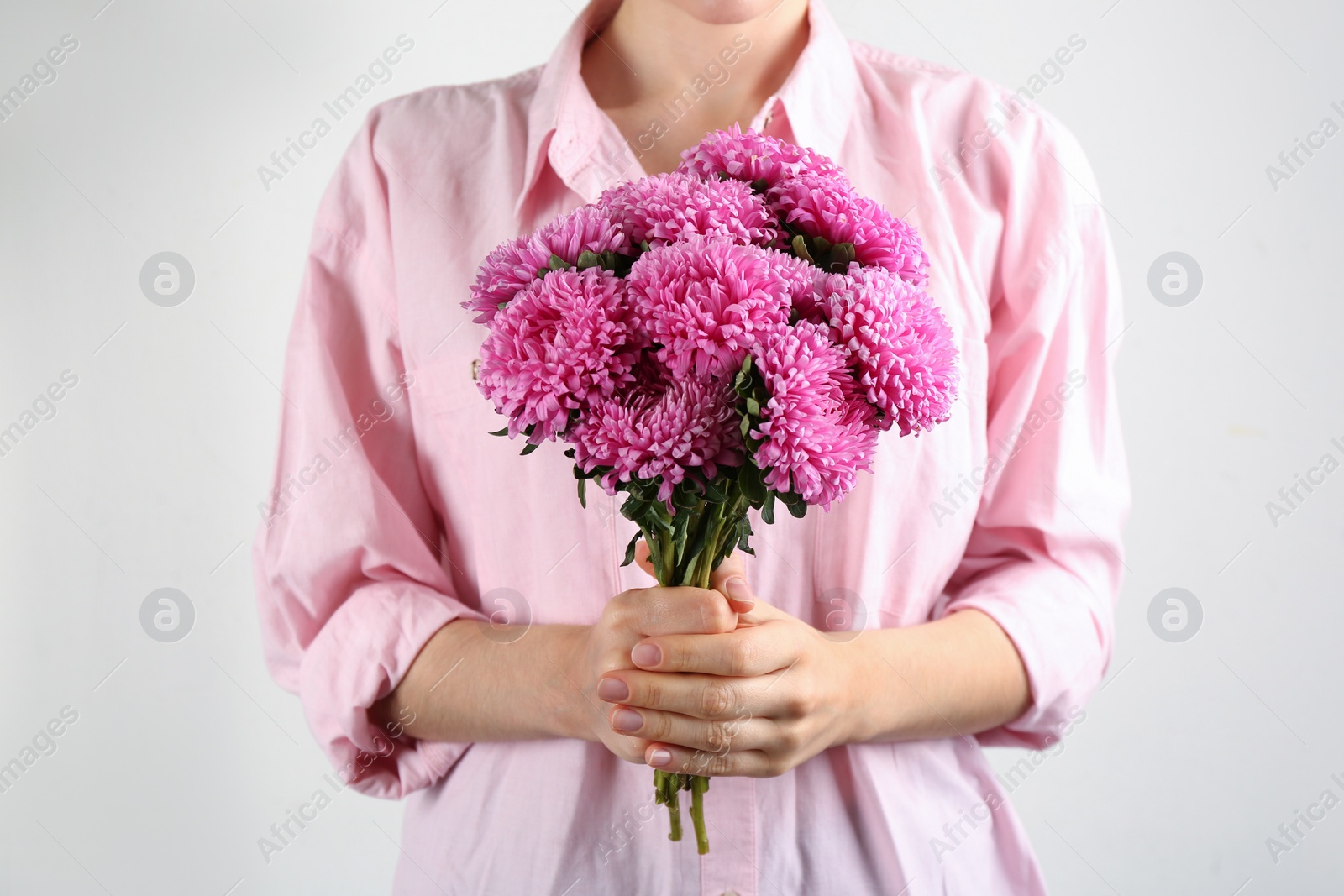 Photo of Woman with bouquet of beautiful asters on light background, closeup. Autumn flowers