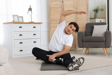 Photo of Overweight man stretching on mat at home