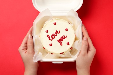 Woman holding takeaway box with bento cake at red table, closeup. St. Valentine's day surprise