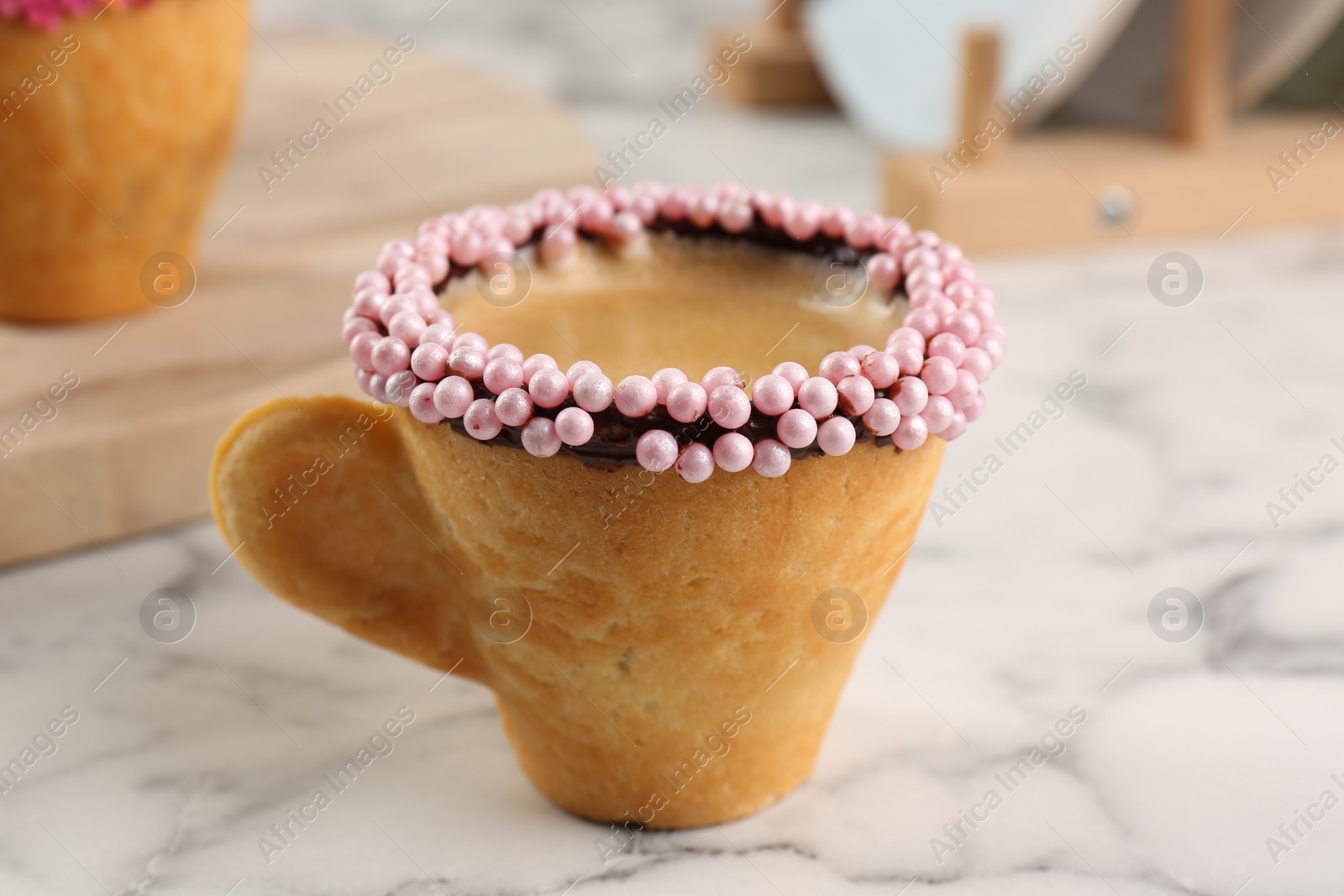 Photo of Delicious edible biscuit cup of coffee decorated with sprinkles on white marble table, closeup