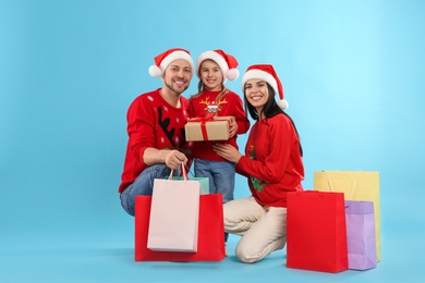 Photo of Happy family with paper bags and gift on light blue background. Christmas shopping