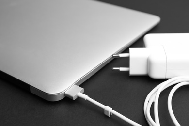 Photo of Laptop and charger on black background, closeup. Modern technology