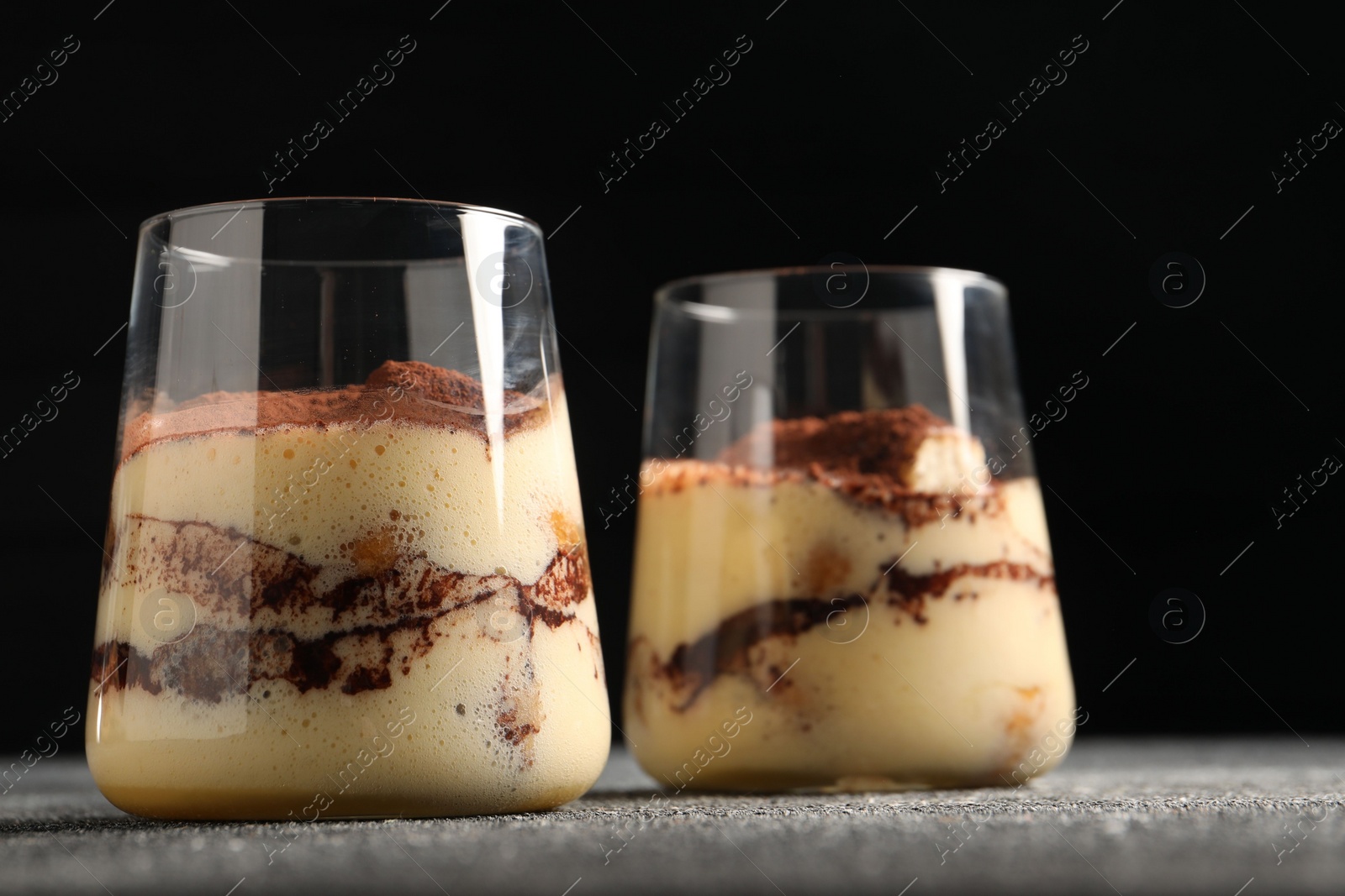 Photo of Delicious tiramisu in glasses on grey textured table, closeup