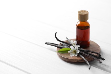 Photo of Vanilla pods, flowers, leaf and bottle with essential oil on white wooden table, closeup. Space for text