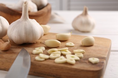 Aromatic cut garlic, cloves and bulbs on white wooden table, closeup