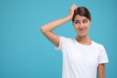 Portrait of embarrassed young woman on light blue background, space for text