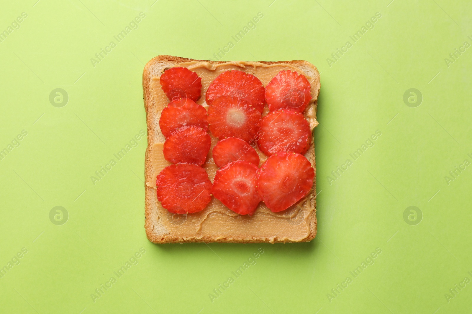 Photo of Tasty peanut butter sandwich with sliced strawberries on light green background, top view