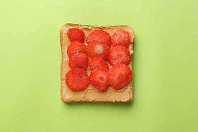 Photo of Tasty peanut butter sandwich with sliced strawberries on light green background, top view