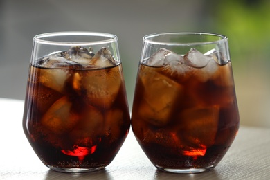 Photo of Glasses of cola with ice on table against blurred background