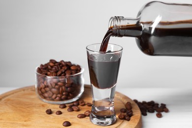 Photo of Pouring coffee liqueur from bottle into glass and beans at light table