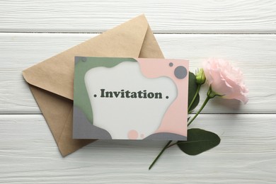 Card with word Invitation, envelope and flowers on white wooden background, flat lay