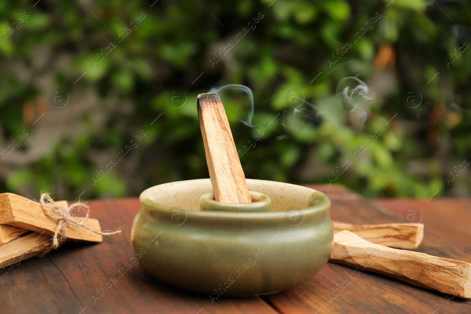 Photo of Palo Santo stick smoldering in holder on wooden table outdoors