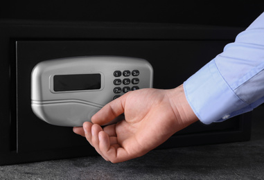Photo of Man opening black steel safe with electronic lock, closeup