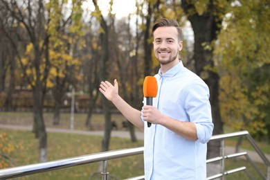 Young male journalist with microphone working in park