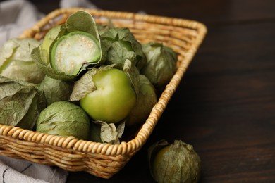 Photo of Fresh green tomatillos with husk in wicker basket on table, closeup