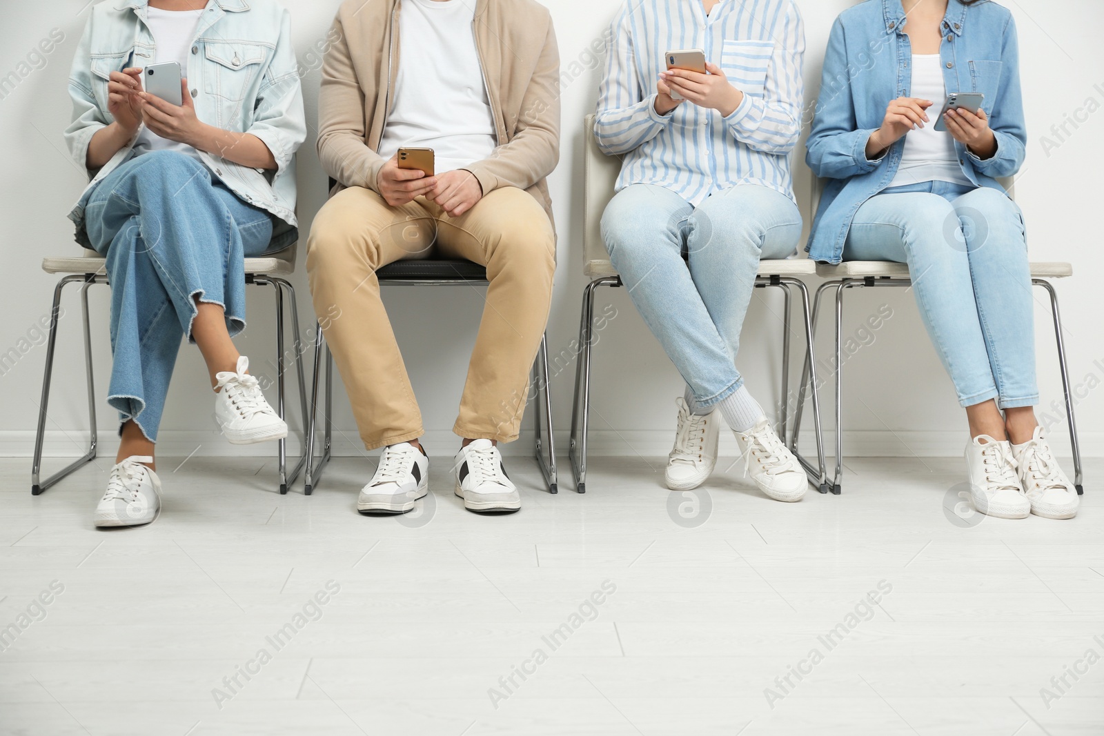 Photo of People with modern smartphones sitting on chairs indoors, closeup