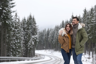 Couple walking near snowy forest, space for text. Winter vacation