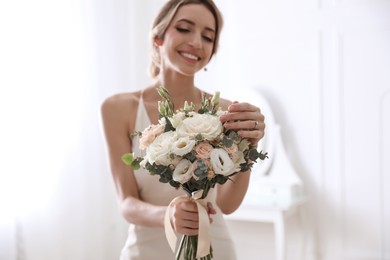 Photo of Young bride with beautiful wedding bouquet in room focus on flowers