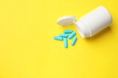 Photo of Vitamin capsules and bottle on yellow background, top view. Space for text