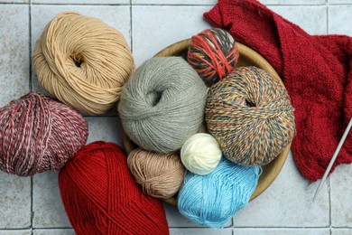 Photo of Soft woolen yarns, knitting and needles on grey tiled background, flat lay